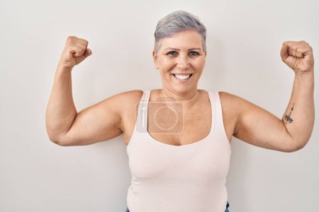 Téléchargez les photos : Middle age caucasian woman standing over white background showing arms muscles smiling proud. fitness concept. - en image libre de droit
