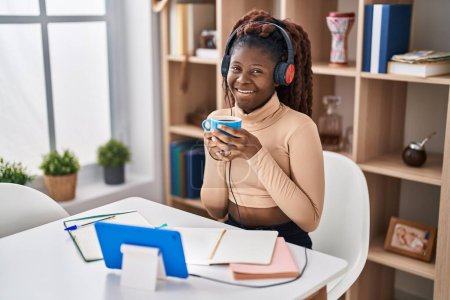 Foto de Estudiante afroamericana escuchando música tomando café en casa - Imagen libre de derechos