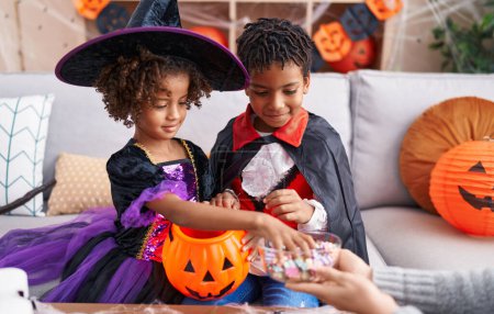 Foto de Adorable afroamericano chico y chica con disfraz de halloween sosteniendo caramelos de bol en casa - Imagen libre de derechos