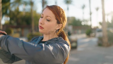 Téléchargez les photos : Jeune rousse femme portant des vêtements de sport regarder chronomètre à la rue - en image libre de droit