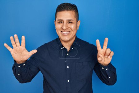 Téléchargez les photos : Jeune homme hispanique debout sur fond bleu montrant et pointant vers le haut avec les doigts numéro huit tout en souriant confiant et heureux. - en image libre de droit
