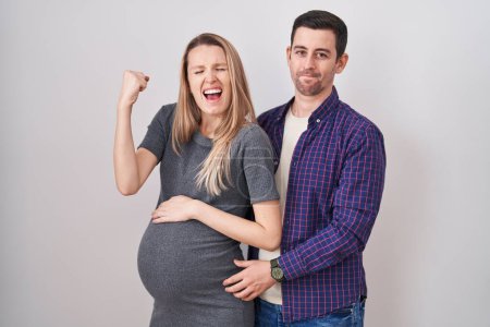 Photo for Young couple expecting a baby standing over white background very happy and excited doing winner gesture with arms raised, smiling and screaming for success. celebration concept. - Royalty Free Image
