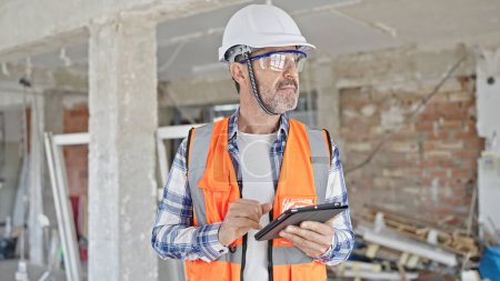 Foto de Constructor de hombre de mediana edad usando touchpad en el sitio de construcción - Imagen libre de derechos