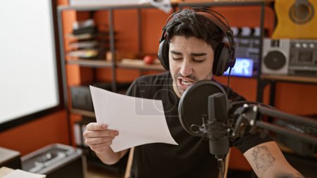 Foto de Joven músico hispano sentado en la mesa cantando canción en el estudio de música - Imagen libre de derechos