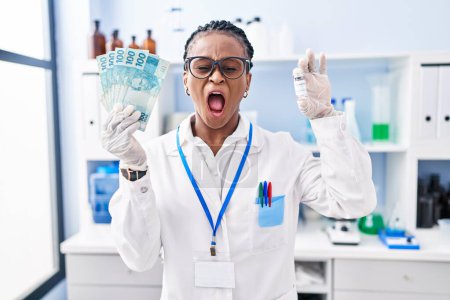 Téléchargez les photos : Femme africaine avec des tresses travaillant au laboratoire scientifique tenant de l'argent en colère et fou hurlant frustré et furieux, criant de colère. rage et concept agressif. - en image libre de droit
