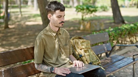 Photo for Young hispanic man tourist using laptop sitting on bench at park - Royalty Free Image