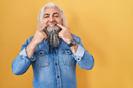 Téléchargez les photos : Homme d'âge moyen avec les cheveux gris debout sur fond jaune souriant avec la bouche ouverte, les doigts pointant et forçant sourire joyeux - en image libre de droit