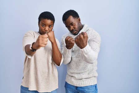 Foto de Joven pareja afroamericana de pie sobre fondo azul juntos listos para luchar con el gesto de defensa del puño, cara enojada y molesta, miedo al problema - Imagen libre de derechos