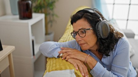 Foto de Mujer hispana de mediana edad escuchando música relajada en el sofá en casa - Imagen libre de derechos