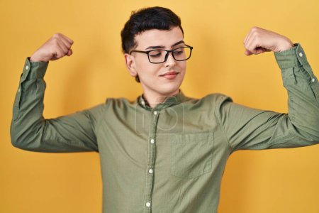 Photo for Non binary person standing over yellow background showing arms muscles smiling proud. fitness concept. - Royalty Free Image