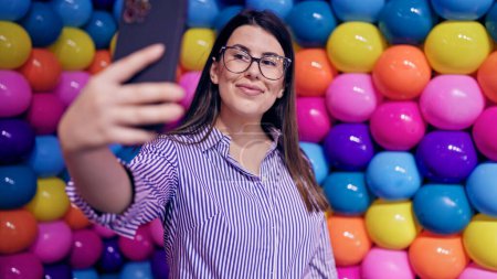 Téléchargez les photos : Jeune belle femme hispanique visitant l'espace d'exposition futuriste coloré prenant selfie - en image libre de droit