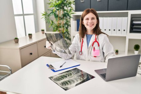 Téléchargez les photos : Jeune femme blonde médecin à la recherche de rayons X assis sur la table à la clinique - en image libre de droit