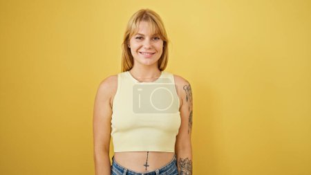 Foto de Joven mujer rubia sonriendo confiada de pie sobre aislado fondo amarillo - Imagen libre de derechos