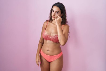 Téléchargez les photos : Jeune femme hispanique portant de la lingerie sur fond rose pointant vers l'œil vous regardant geste, expression suspecte - en image libre de droit
