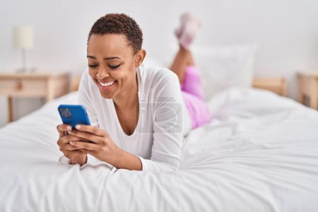 Téléchargez les photos : African american woman using smartphone lying on bed at bedroom - en image libre de droit