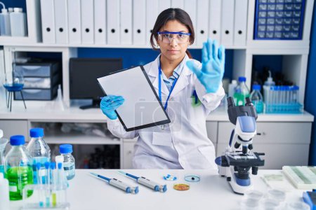 Photo for Hispanic young woman working at scientist laboratory doing stop sing with palm of the hand. warning expression with negative and serious gesture on the face. - Royalty Free Image