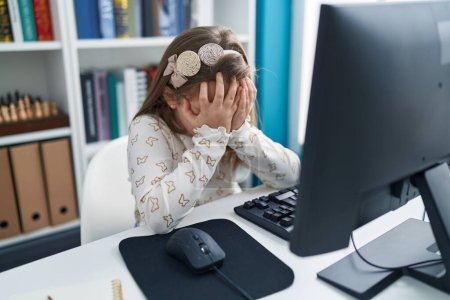 Foto de Adorable chica rubia estudiante estresado utilizando la computadora en el aula - Imagen libre de derechos