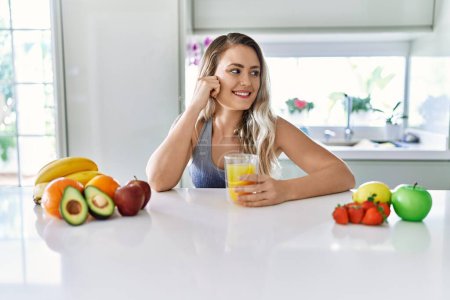 Téléchargez les photos : Young woman smiling confident holding orange juice at kitchen - en image libre de droit