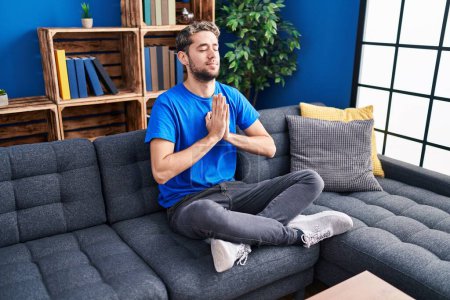 Photo for Young man doing yoga exercise sitting on sofa at home - Royalty Free Image