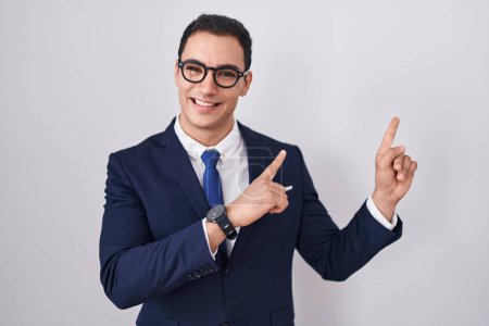 Photo for Young hispanic man wearing suit and tie smiling and looking at the camera pointing with two hands and fingers to the side. - Royalty Free Image