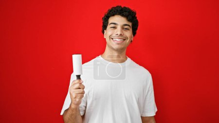 Photo for Young latin man holding stick roll to clean pet hair smiling over isolated red background - Royalty Free Image