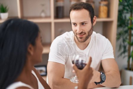 Téléchargez les photos : Man and woman interracial couple drinking wine sitting on table at home - en image libre de droit