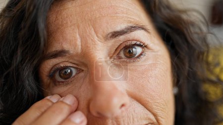 Foto de Mujer hispana de mediana edad tocando los ojos holgados en casa - Imagen libre de derechos