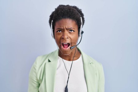 Photo for African american woman wearing call center agent headset angry and mad screaming frustrated and furious, shouting with anger. rage and aggressive concept. - Royalty Free Image