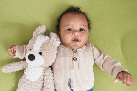 Photo for African american baby relaxing on bed with teddy bear at bedroom - Royalty Free Image