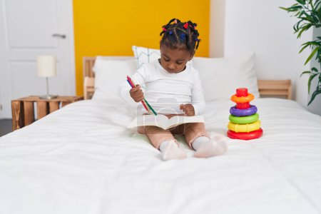 Foto de Chica afroamericana sentada en la cama dibujo en el cuaderno en el dormitorio - Imagen libre de derechos