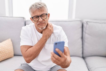 Téléchargez les photos : Homme aux cheveux gris d'âge moyen ayant une téléconsultation assis sur le canapé à la maison - en image libre de droit