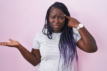 Photo for Young african woman standing over pink background confused and annoyed with open palm showing copy space and pointing finger to forehead. think about it. - Royalty Free Image