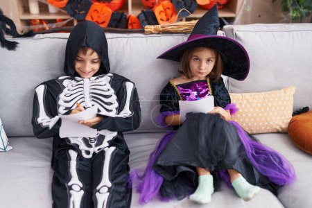 Foto de Adorable niño y niña con el traje de Halloween dibujo en papel en casa - Imagen libre de derechos