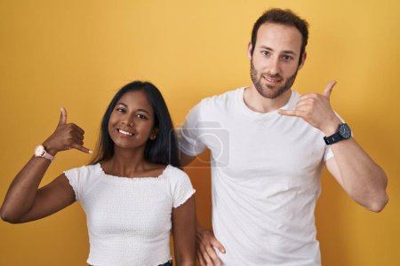 Téléchargez les photos : Couple Interracial debout sur fond jaune souriant faire geste téléphonique avec la main et les doigts comme parler au téléphone. communiquer les concepts. - en image libre de droit