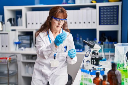 Téléchargez les photos : Femme scientifique d'âge moyen mesurant le liquide au laboratoire - en image libre de droit