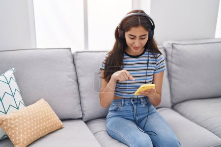 Foto de Joven chica hispana escuchando música sentada en el sofá en casa - Imagen libre de derechos