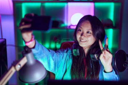 Téléchargez les photos : Young chinese woman streamer smiling confident make selfie by smartphone at gaming room - en image libre de droit