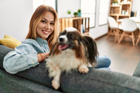 Photo for Young caucasian woman smiling confident sitting on sofa with dog at home - Royalty Free Image
