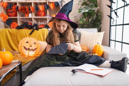 Téléchargez les photos : Adorable fille blonde portant costume de sorcière couper du papier chauve-souris à la maison - en image libre de droit