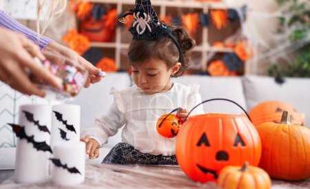 Photo for Adorable hispanic girl wearing halloween costume holding pumpkin basket at home - Royalty Free Image
