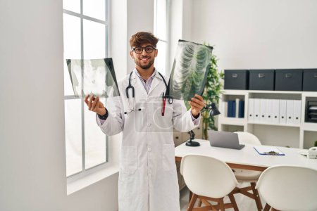 Téléchargez les photos : Jeune homme arabe portant un uniforme de médecin tenant des rayons X à la clinique - en image libre de droit