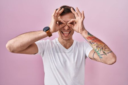 Photo for Caucasian man standing over pink background doing ok gesture like binoculars sticking tongue out, eyes looking through fingers. crazy expression. - Royalty Free Image
