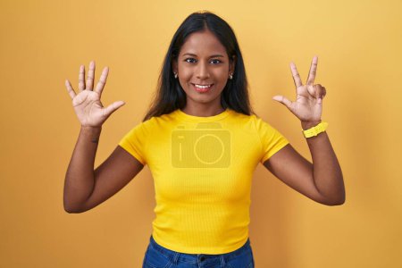 Photo for Young indian woman standing over yellow background showing and pointing up with fingers number eight while smiling confident and happy. - Royalty Free Image