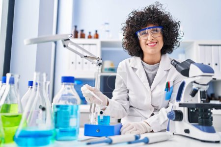Foto de Joven científica de Oriente Medio sonriendo confiada midiendo líquido en laboratorio - Imagen libre de derechos