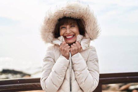 Foto de Middle age woman smiling confident freezing at seaside - Imagen libre de derechos