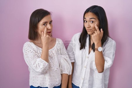 Téléchargez les photos : Mère et fille hispaniques pointant ensemble vers l'œil vous regardant geste, expression suspecte - en image libre de droit