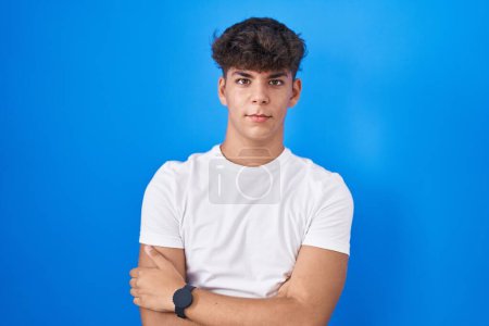 Photo for Hispanic teenager standing over blue background skeptic and nervous, disapproving expression on face with crossed arms. negative person. - Royalty Free Image