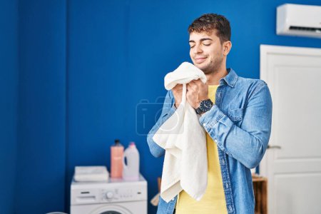 Téléchargez les photos : Young hispanic man smelling towel standing at laundry room - en image libre de droit