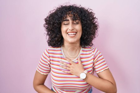 Téléchargez les photos : Jeune femme du Moyen-Orient debout sur fond rose souriant et riant fort à haute voix parce que drôle blague folle avec les mains sur le corps. - en image libre de droit