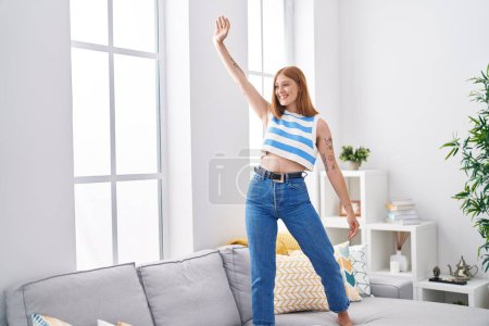Téléchargez les photos : Jeune rousse femme souriante danse confiante sur le canapé à la maison - en image libre de droit